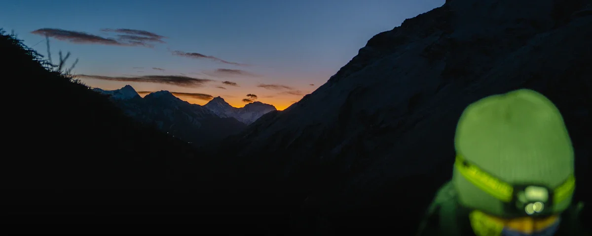 کوهنورد مجهز به هدلامپ در مسیر کوهستان هنگام غروب